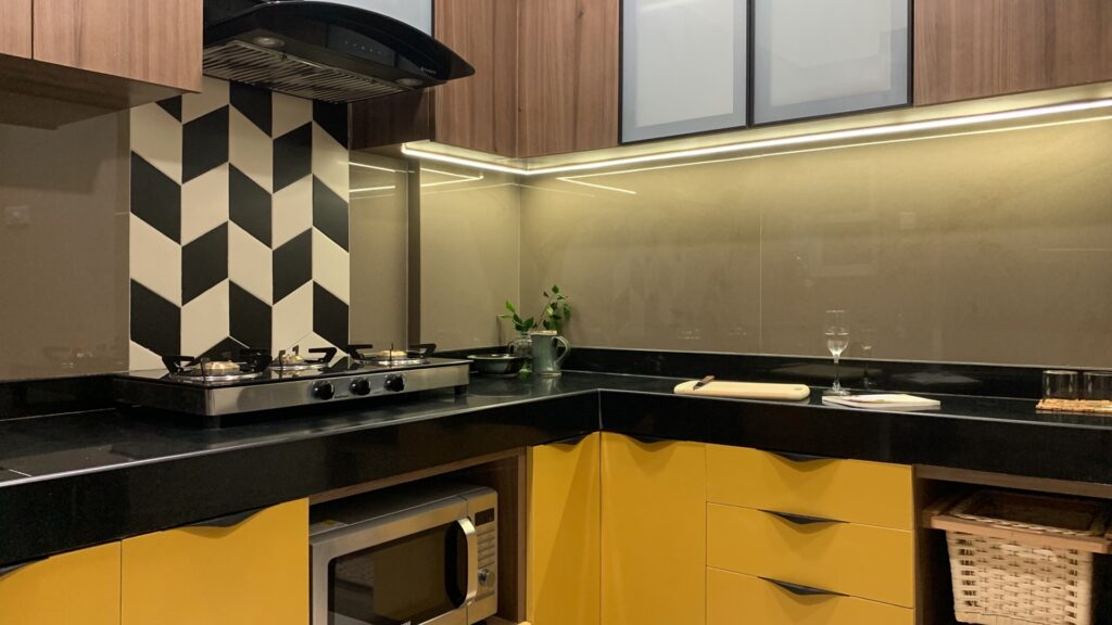 Small kitchen interiors featuring mustard and walnut cabinets with wicker baskets for maximum storage, black countertop, accent backsplash tiles and functional lighting
