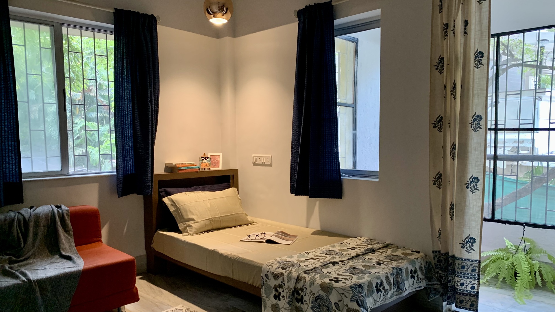 Bedroom interiors with a low bed, navy curtains, Indian fabrics, pendant light and red accent sofa for rental apartments