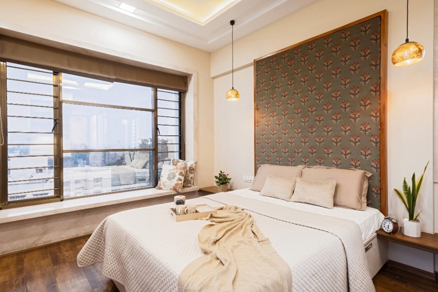 Cozy modern bedroom interior with large window seating, Indian motif headboard panel, pendant lighting, wooden flooring, and soft neutral décor designed and executed by New Leaf Designs Pune